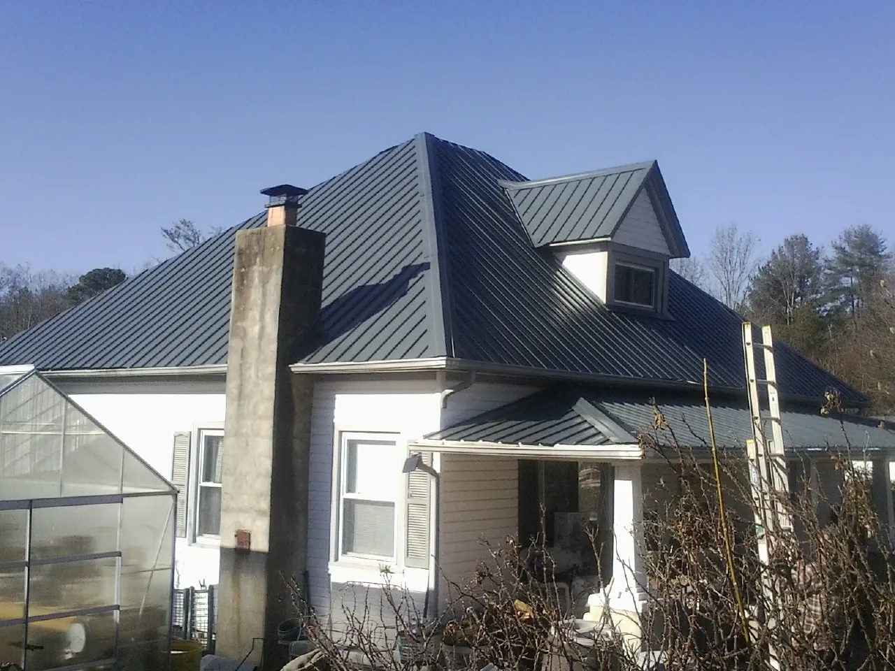 Dark blue standing seam metal roof on a white farmhouse with dormer — Slate & Tile Roof Repair by Roofing Brothers in Maplewood