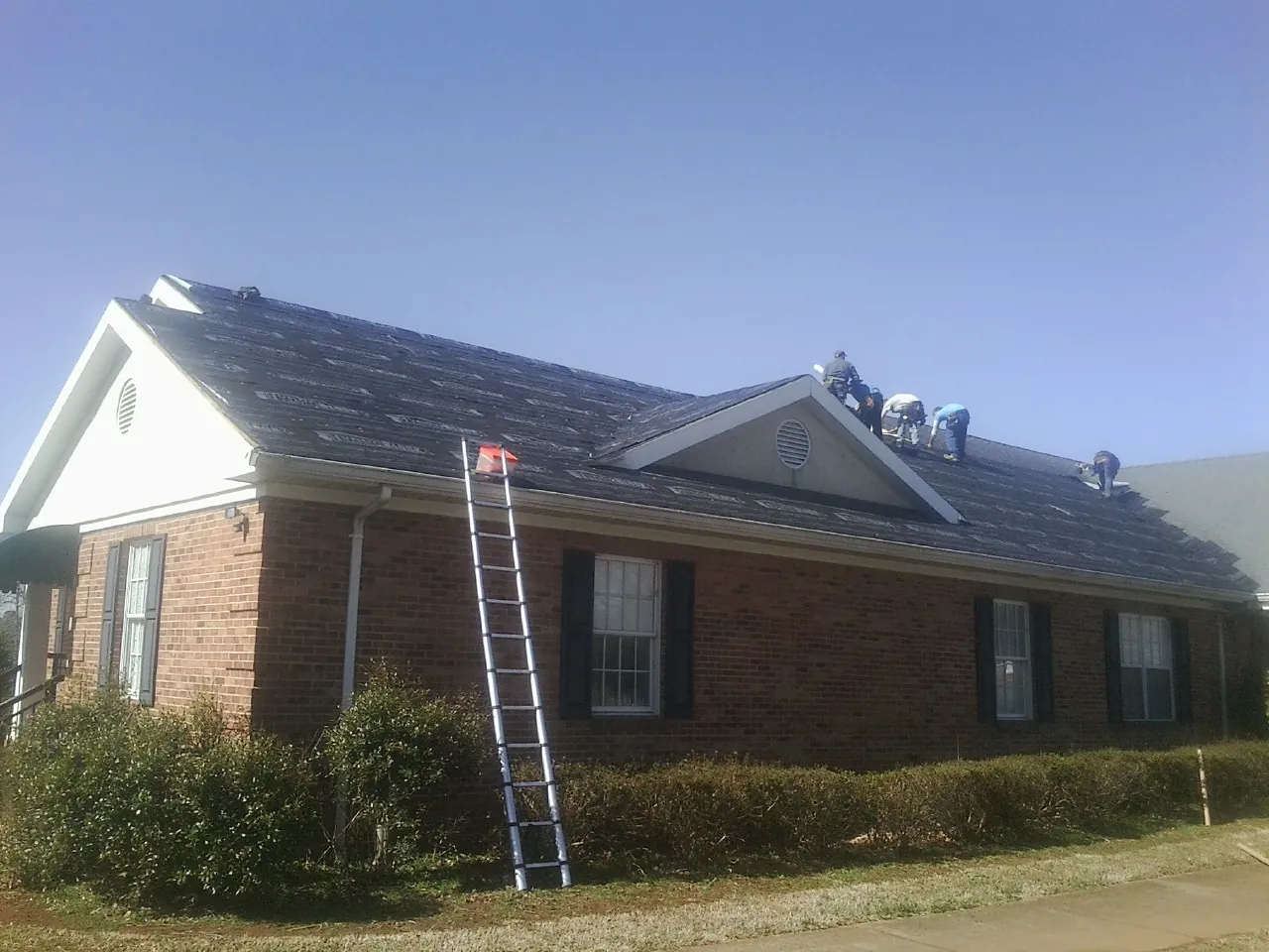 Crew tearing shingles off a brick ranch roof with a ladder set — Emergency Roof Repair work by our crew in Maplewood