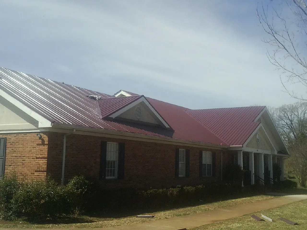 Red metal roof with gabled entries on a long brick building, from a Hail Damage Roof Repair job in Maplewood