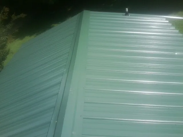 New green metal panels meeting at the ridge of a roof — Flat Roof Repair work by our crew in Maplewood