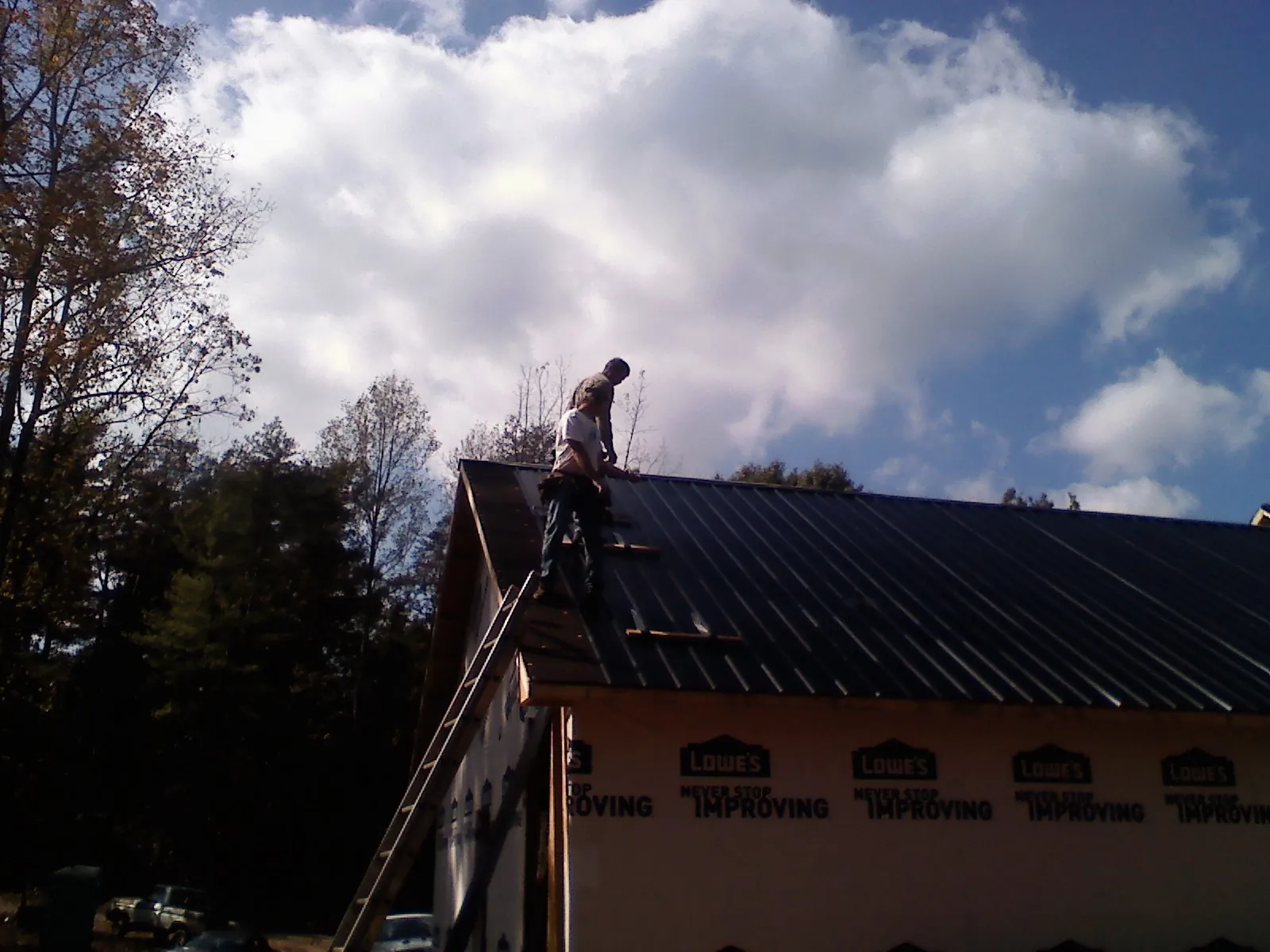 Roofer fastening dark metal panels high against a cloudy sky, from a Roof Inspection job in Maplewood
